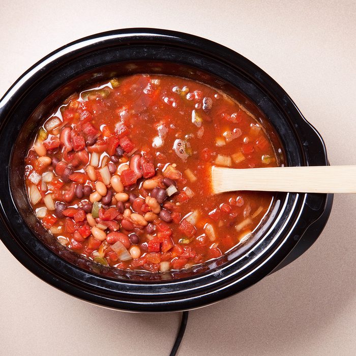 An overhead view of vegetarian chili with a spoon in a slow cooker.