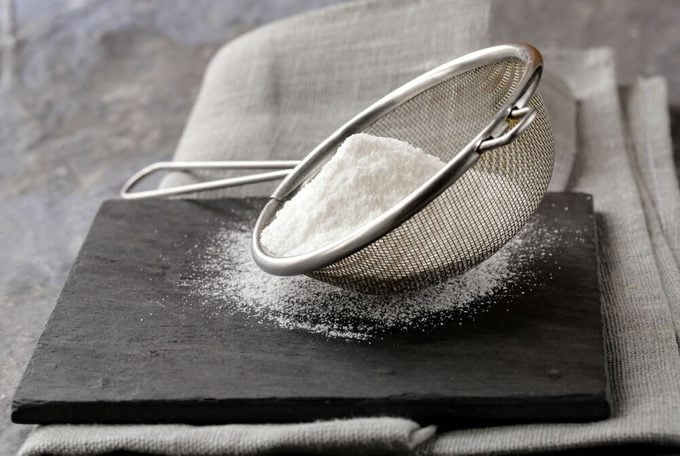 powdered sugar in a metal strainer on a gray background