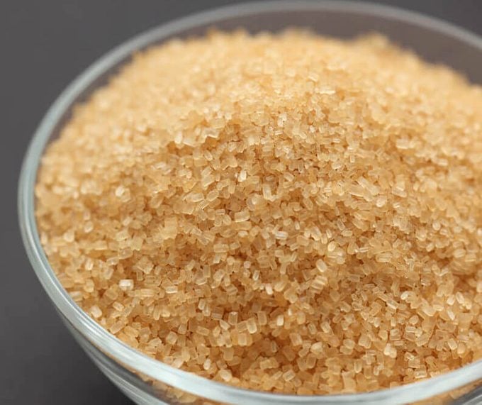 Brown cane sugar in a glass bowl on black background. Shallow depth of field. Closeup