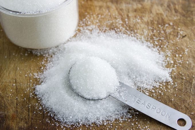 granulated sugar in spoon and sugar pile on wooden