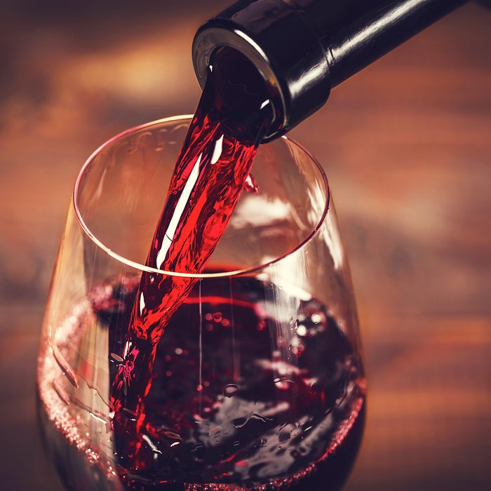 Pouring red wine into the glass against wooden background; Shutterstock ID 370977980