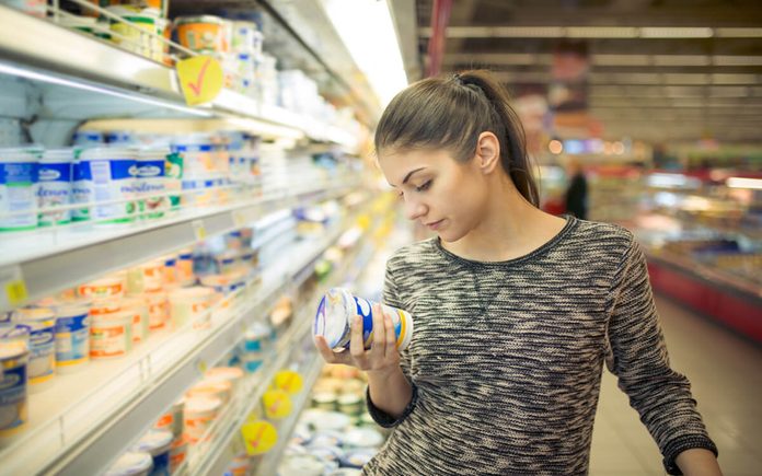 Young woman reading ingredients,declaration or expiration date on a dairy product before buying it.Curious woman reading nutritional values of the food.Shopping in the supermarket grocery store