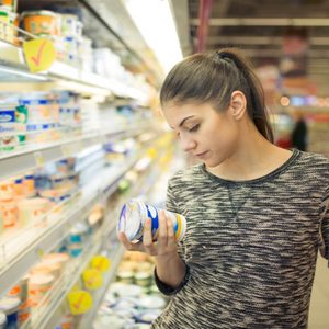 Young woman reading ingredients,declaration or expiration date on a dairy product before buying it.Curious woman reading nutritional values of the food.Shopping in the supermarket grocery store