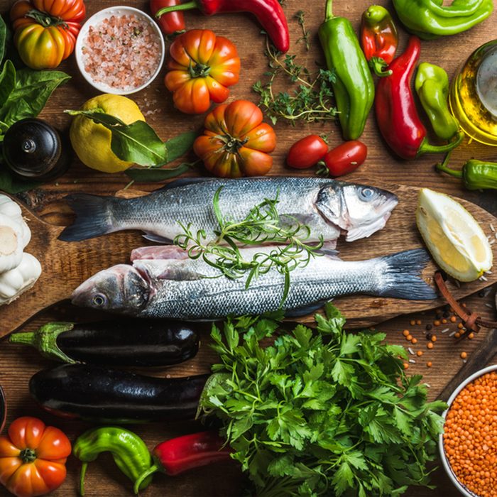 Raw uncooked seabass fish with vegetables, grains, herbs and spices on chopping board over rustic wooden background, top view; Shutterstock ID 415721434