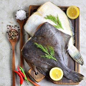 Raw fish flatfish on a wooden board with lemon and spices gray background. copy Space