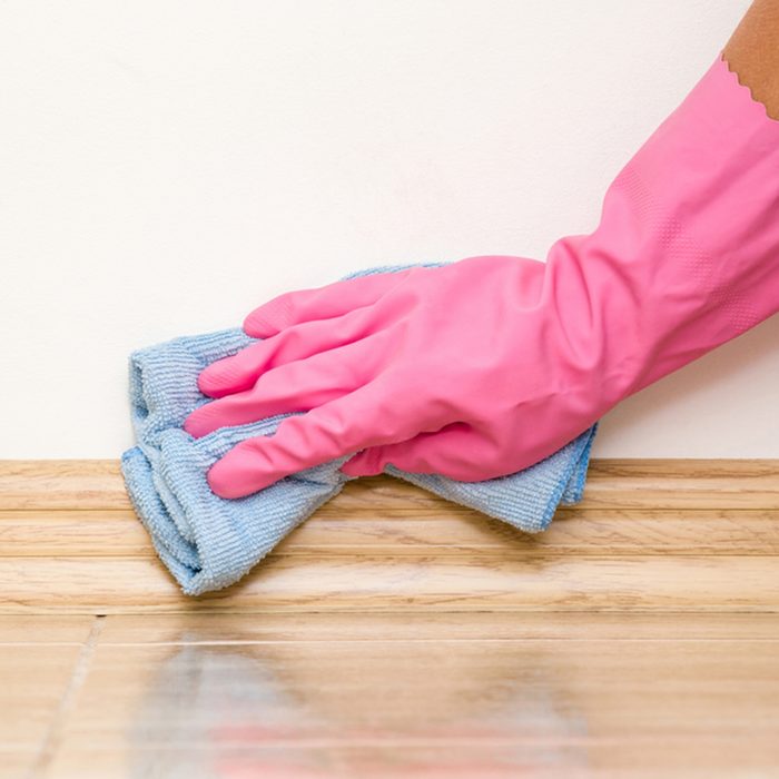 Hand in rubber protective glove cleaning baseboard on the floor from dust with microfiber rag at the wall. Early spring cleaning or regular clean up. Maid cleans house.; Shutterstock ID 664596868