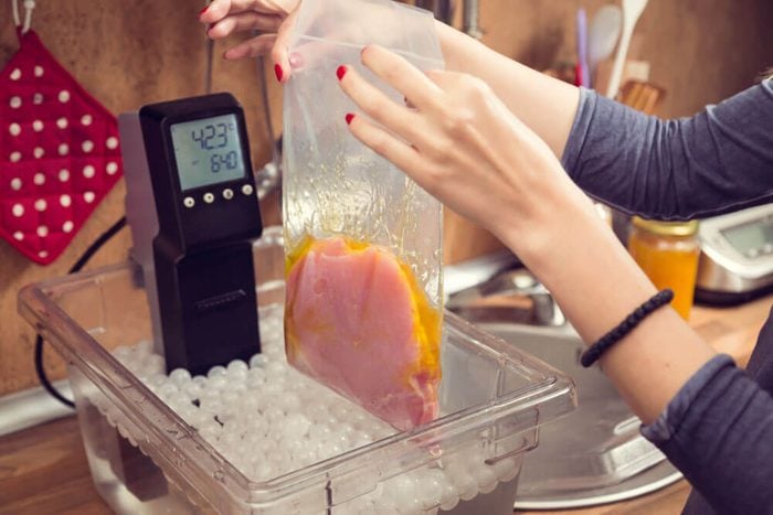 Sous vide cooking. Woman putting meat fillet in sous vide cooker.