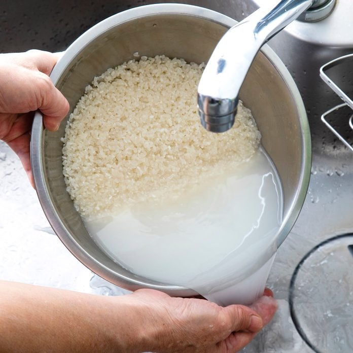 A person rinsing a pot of white rice in the sink.