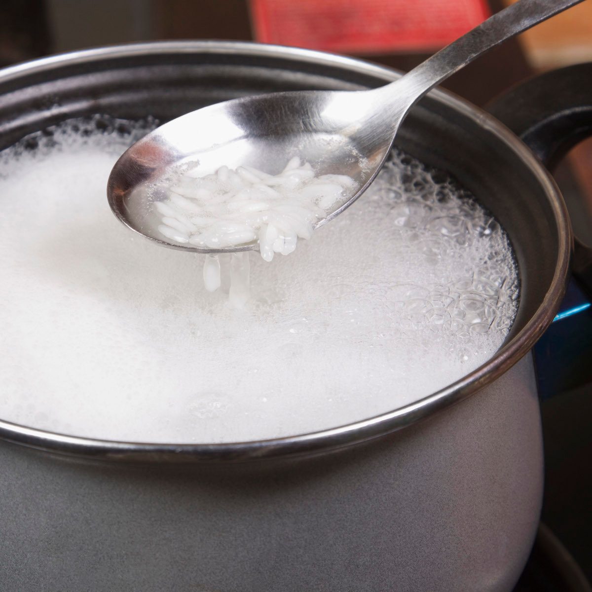 A spoonful of rice over a pot of boiling rice.