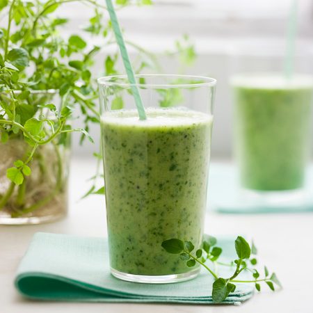 Two glasses of a healthy green smoothie herb drink with a straw.