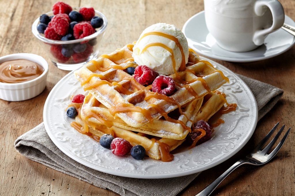 Plate of belgian waffles with ice cream, caramel sauce and fresh berries