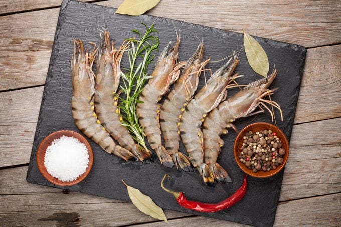 Fresh raw tiger prawns and spices on black stone plate over wooden table