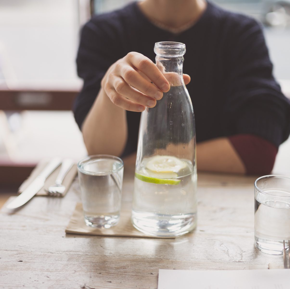 A young woman is sitting at a table in a restaurant and is drinking water