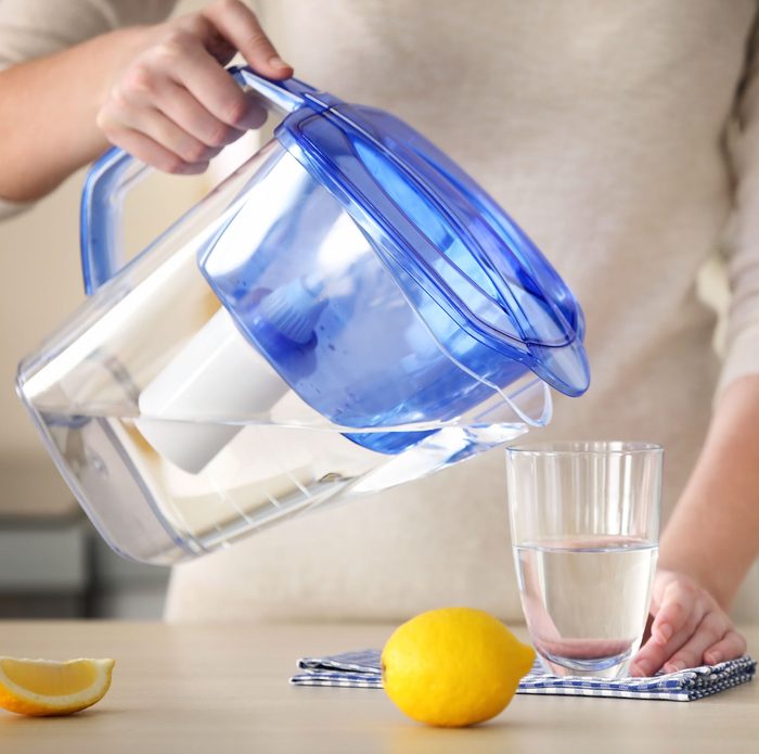 Woman pouring water from filter jug into glass in the kitchen