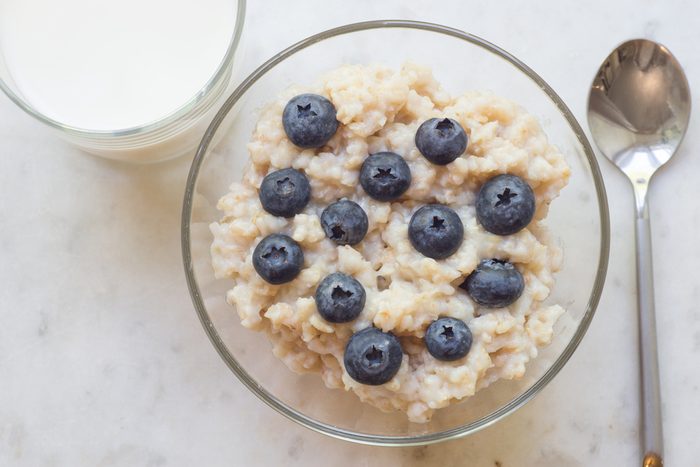 Bowl of oatmeal porridge with blueberry on marble table, with glass of milk, hot and healthy breakfast every day, diet food