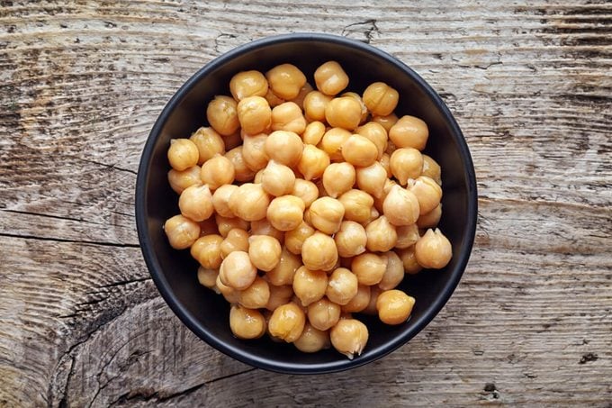 Black bowl of preserved chickpeas on wooden table, top view