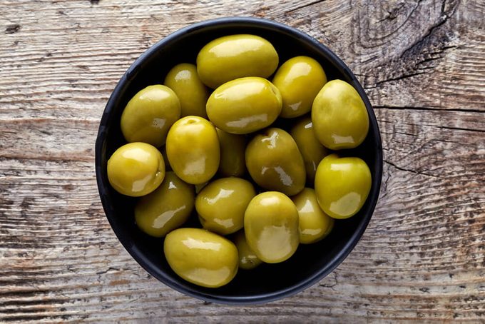 Bowl of pickled olives on wooden background, top view