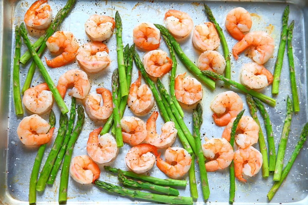 Sheet pan dinner of shrimp and asparagus with olive oil and black pepper.