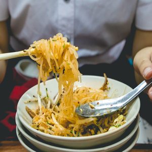 A girls eating Chinese food (noodles)with sticks.