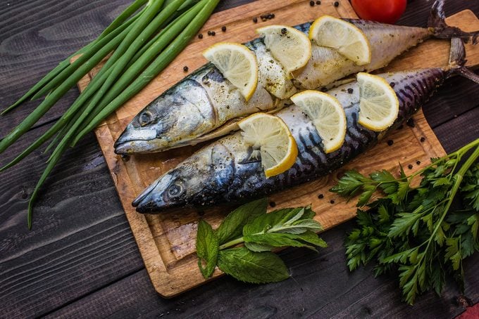 Fish dish cooking with various ingredients. Raw mackerel with lemon, garlic, herbs and spices on cutting board, top view. Healthy food or diet nutrition concept