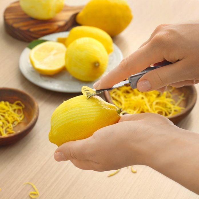Woman taking off lemon peel with zester over table; Shutterstock ID 691820386; Job (TFH, TOH, RD, BNB, CWM, CM): Taste of Home