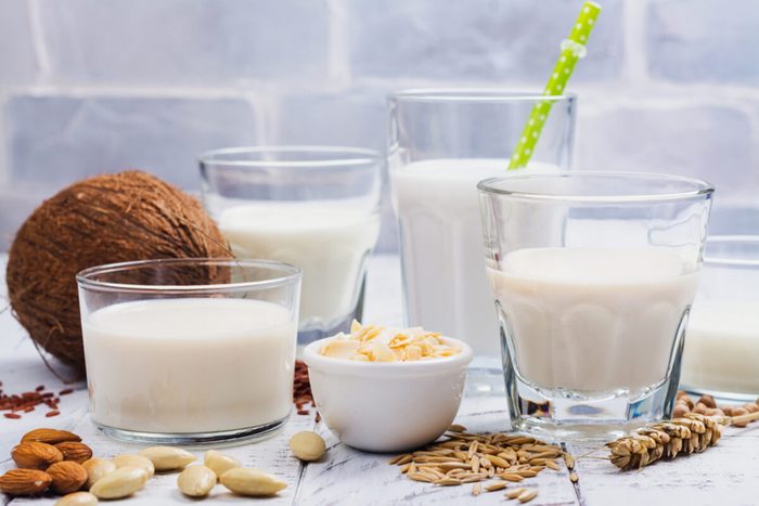 Assortment of non dairy vegan milk and ingredients on white wooden background.