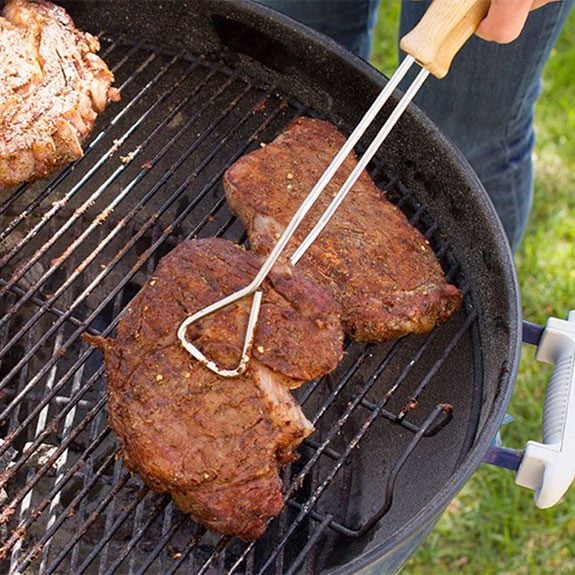 Picking up steak on grill with tongs