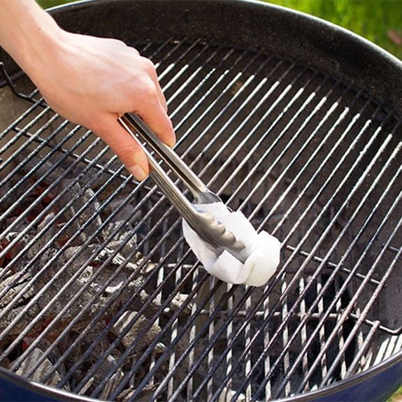 Wiping grill with paper towel in tongs
