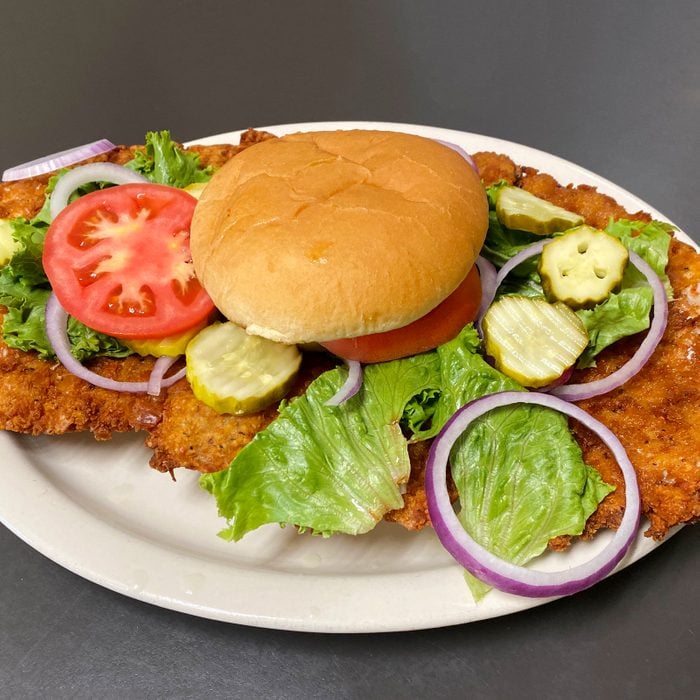fried pork tenderloin sandwich on a paper plate. The pork is much larger than the bun and taking up the whole plate