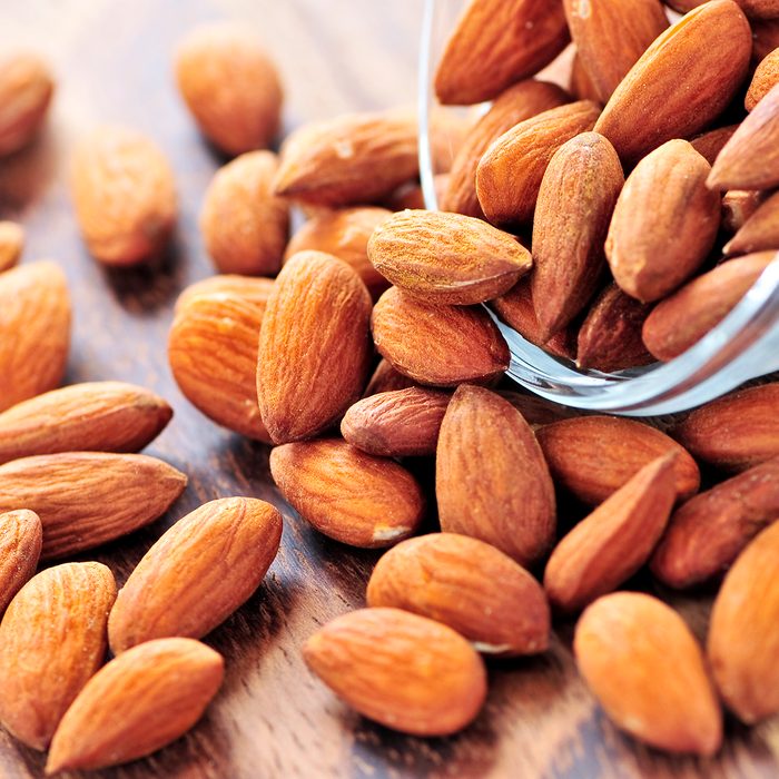 Raw almonds spilling out of small glass bowl