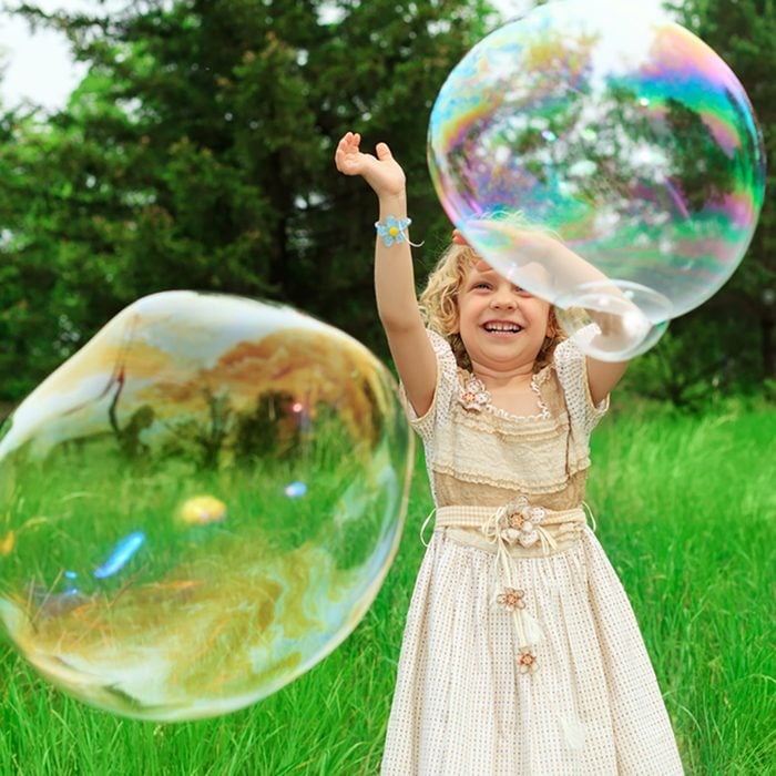 Pretty little girl is playing with big bubbles in a park