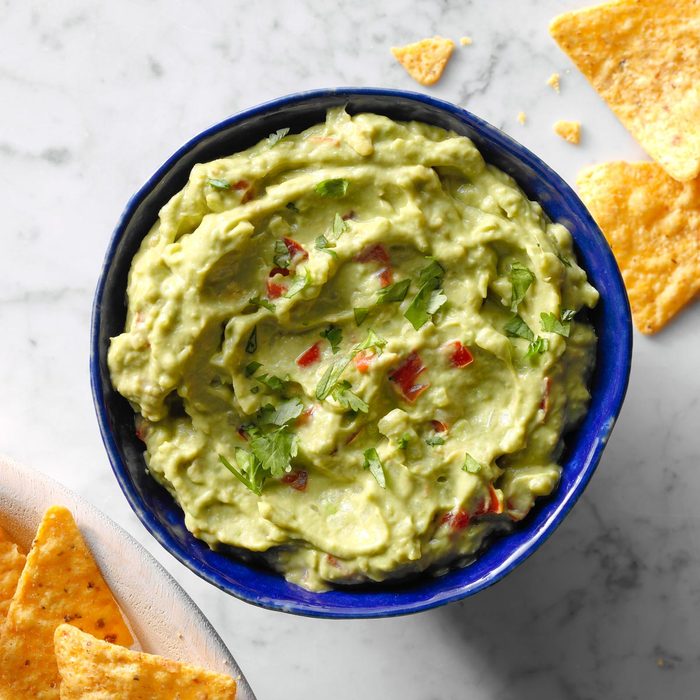 Guacamole in a blue bowl with a few tortilla chips surrounding on a marble surface