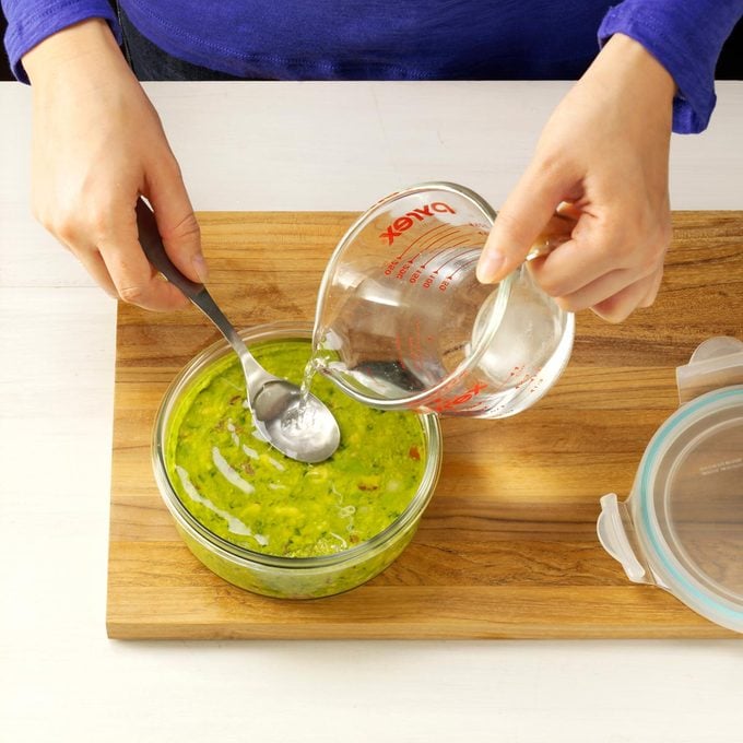 person adding water to the top of a container of guacamole