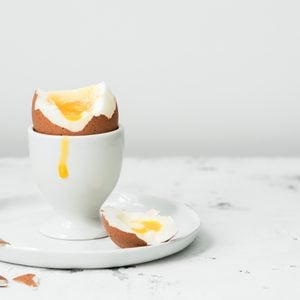 Soft-boiled egg in eggcup with yolk on white stone table.