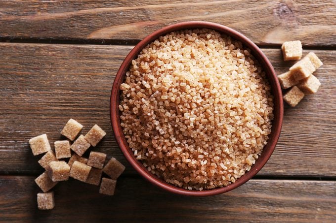 Brown sugar cubes and crystal sugar in bowl on wooden background