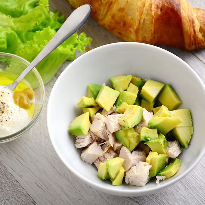 Preparing chicken avocado salad with light yogurt dressing on gray wooden table.