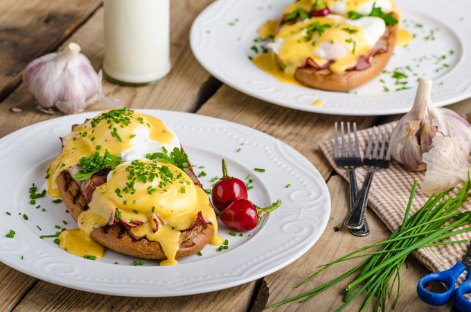 Eggs Benedict with little salad, milk and fresh herbs