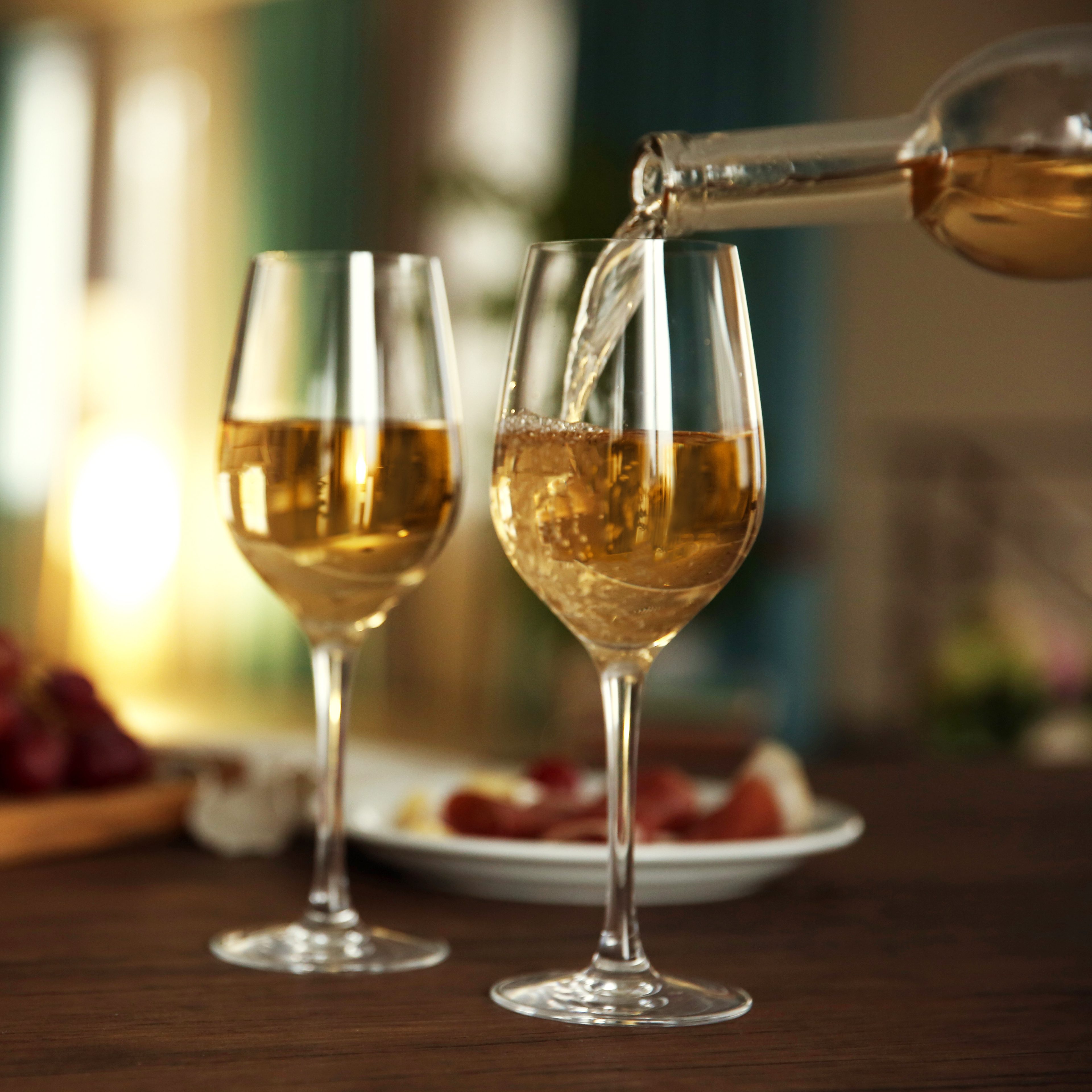 Pouring white wine from bottle into the wineglass on the table over blurred background
