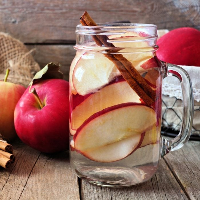 Autumn themed detox water with apple, cinnamon and red pear in a mason jar. Scene on rustic wood background