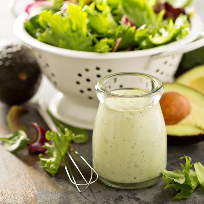 Avocado ranch dressing in small jar with salad leaves in a colander.