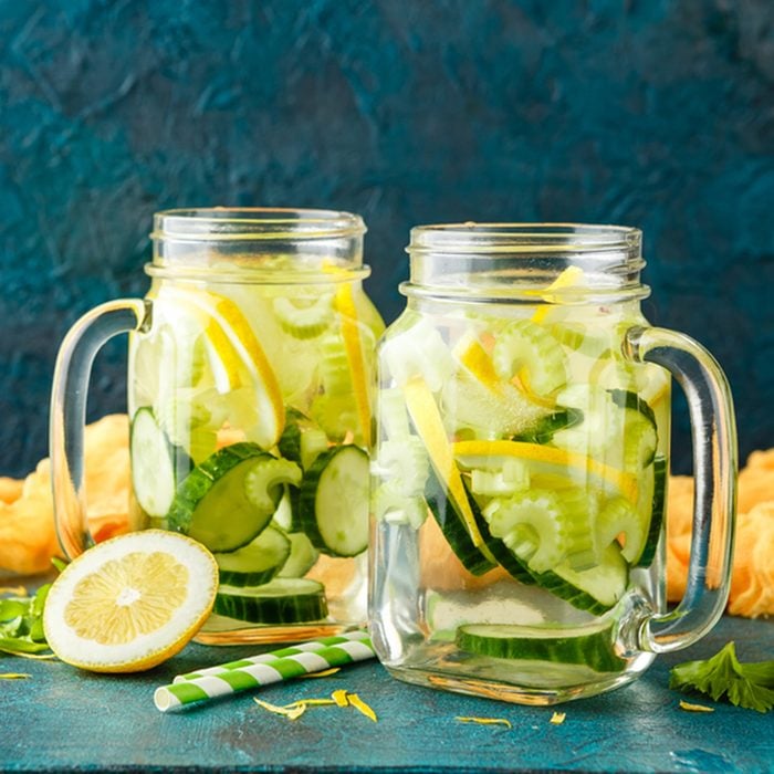 Detox infused hydrating water with cucumber, lemon and celery in glass jars on a turquoise background