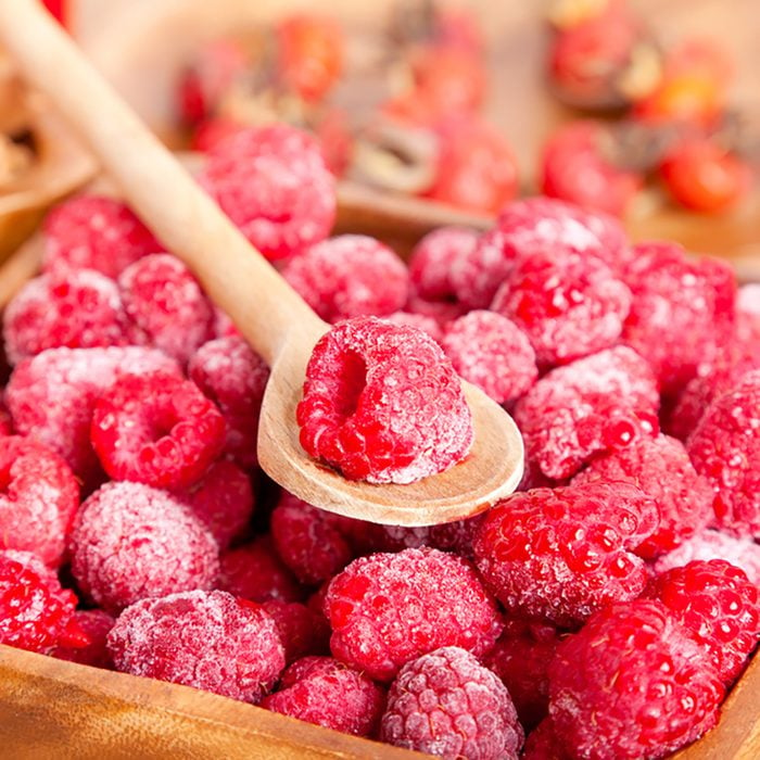 frozen raspberries in the wooden bowl with spoon.