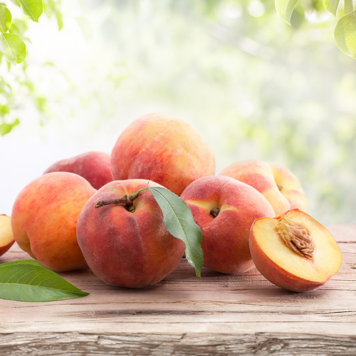 Ripe peaches with leaves on a wooden board on a background of green leaves; Shutterstock ID 682256068