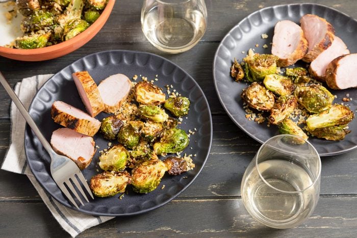 Air Fryer Brussels Sprouts Served in Black Plates With Meat Pieces on Wooden Surface