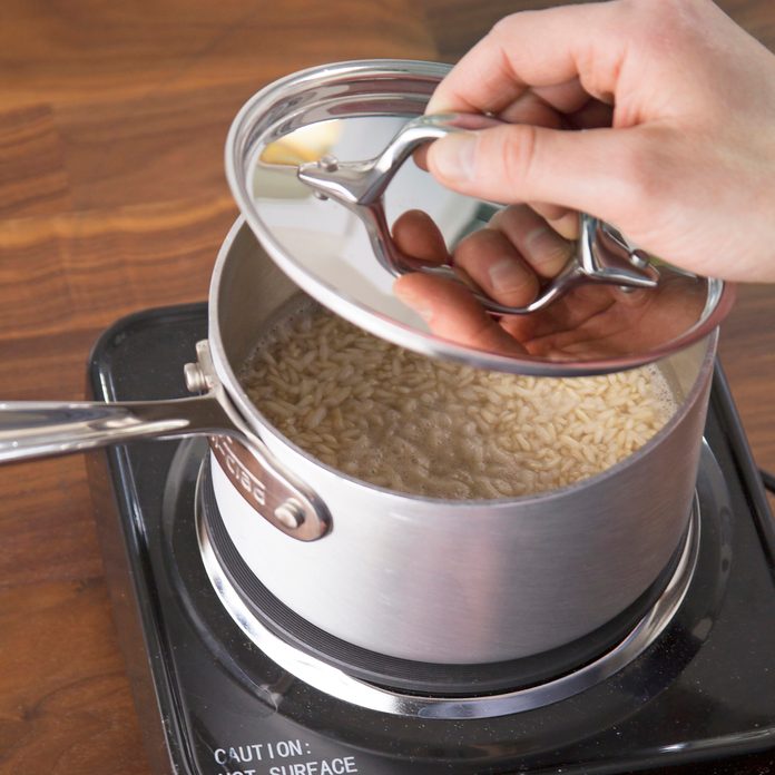A person placing the lid on a pot of rice to let it simmer on the stovetop.