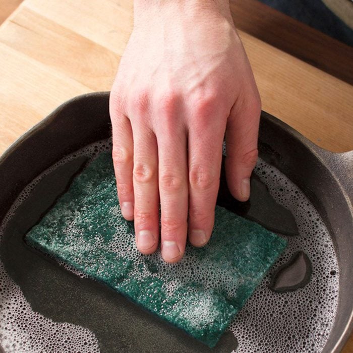 Hand pushing a sponge into a water-filled skillet