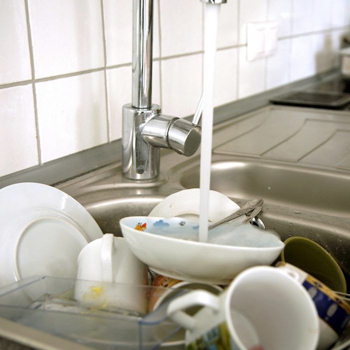 Pile of dirty dishes in the metal sink and pouring tap water.