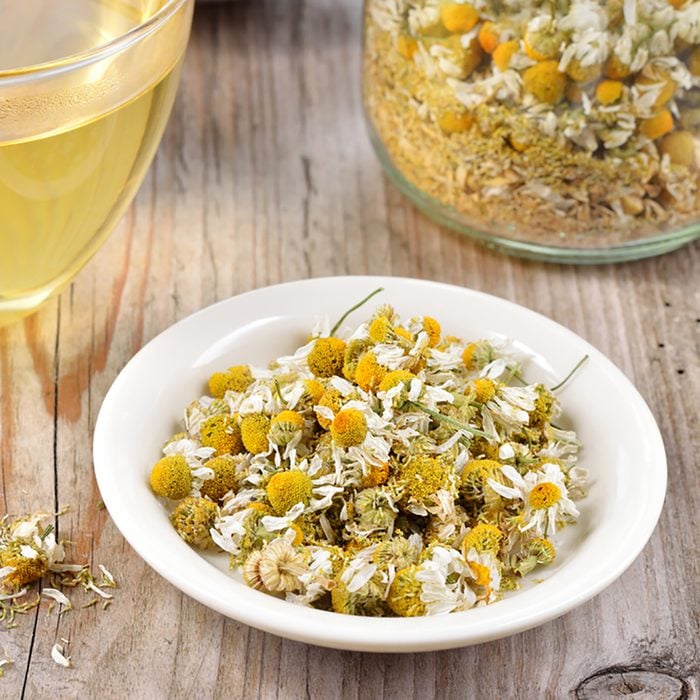 Dried camomile flowers on saucer. Chamomile tea in a transparent cup and dried camomile flowers on wooden table. Herbal tea for baby's stomach.; Shutterstock ID 222521101