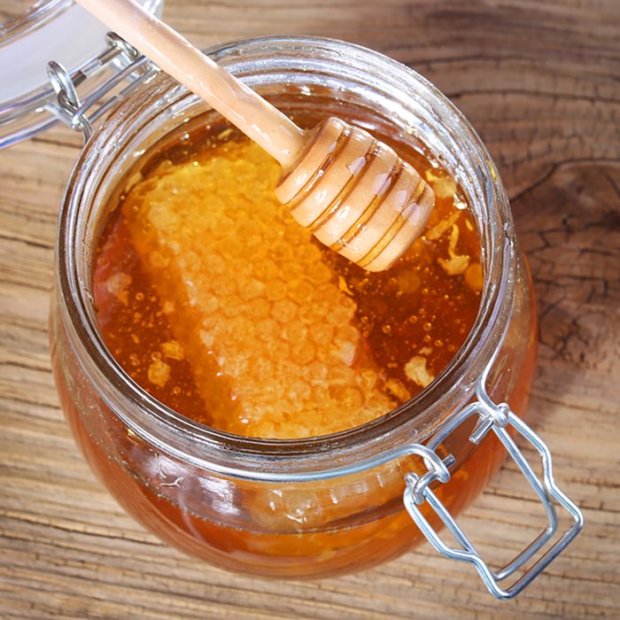Jar of honey with honeycomb and dipper on wooden background