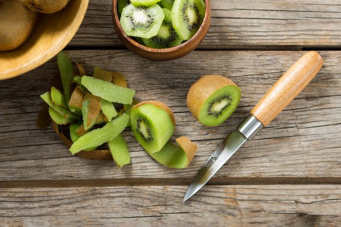 Overhead of sliced kiwi and pile of kiwi skin on wooden table